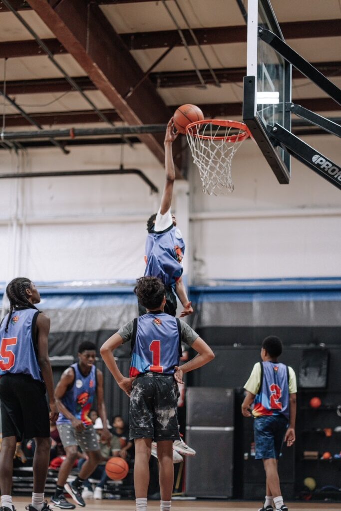 Player finishing a layup above the rim as teammates watch from the court.